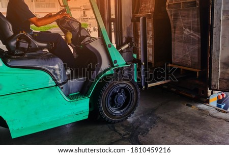 Worker driving forklift loading shipment carton boxes goods on wooden pallet at loading dock from container truck to warehouse cargo storage in freight logistics, transportation industrial, delivery