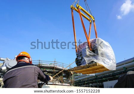 Worker during rope access rigger commencing high risk job to holding a safety tag line rope to control a load while crane, boom truck, truck loader is lifting transformers unit in chemical plant.