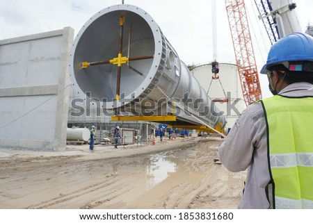 Worker during rope access rigger commencing high risk job to holding a safety tag line rope to control a load while crane, boom truck, truck loader is lifting transformers unit in chemical plant.