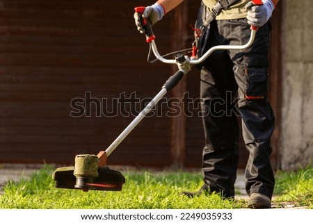 Worker with electric mower in his hands, mowing grass in front of the house.