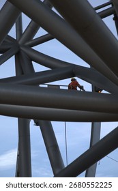 Worker in elevated work platform using exothermic cutting torch to dismantle large metal structure, wearing protective safety gear including hard hat and protective suit.