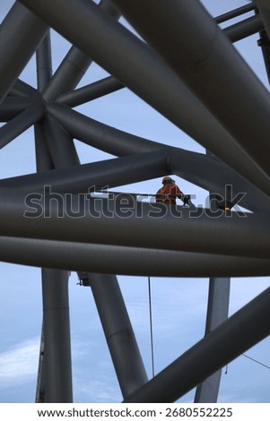 Worker in elevated work platform using exothermic cutting torch to dismantle large metal structure, wearing protective safety gear including hard hat and protective suit.