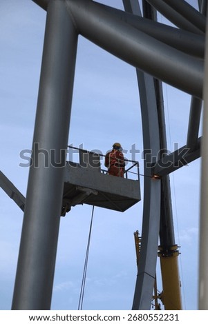 Worker in elevated work platform using exothermic cutting torch to dismantle large metal structure, wearing protective safety gear including hard hat and protective suit.