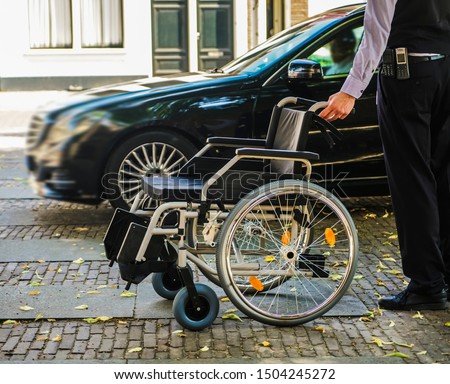 worker - employee greets a disabled person who came by taxi. hotel service. car parking near entrance. no face. 