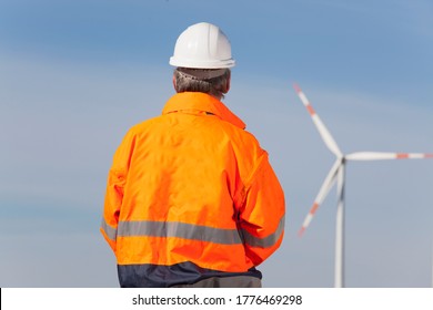 Worker or engineer with hard hat and protecive clothing looking at a windmill of a windfarm - focus on the man