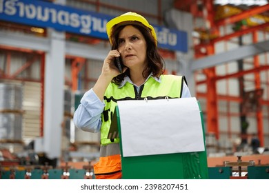 worker or engineer talking on smartphone and looking information on clipboard in the factory