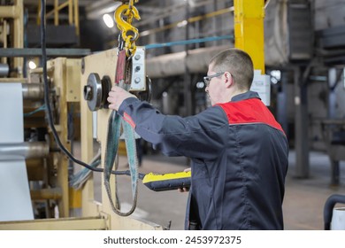 A worker at a factory turns on the installation of an overhead crane to lift a load. - Powered by Shutterstock