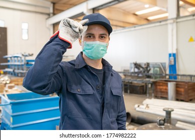 Worker In A Factory Wearing A Mask And Holding His Protective Hat