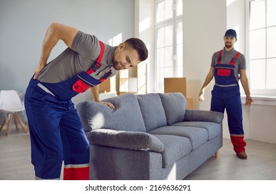 Worker feels sudden pain in his lower back when he tries to lift a heavy sofa. Two young men from a delivery service or a moving company can't carry a heavy couch because one of them gets injured - Shutterstock ID 2169636291