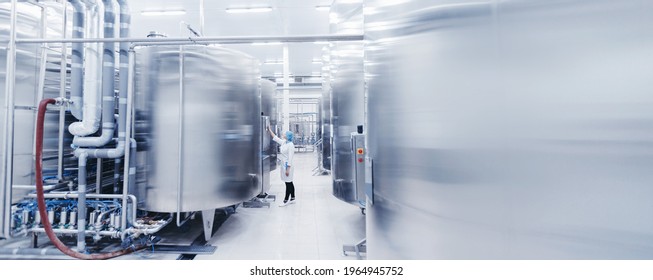 Worker female engineer operator in uniform uses process control panel food factory production line and steel tanker. - Shutterstock ID 1964945752