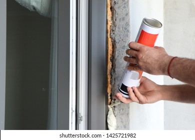 The worker fills the gap between the window and the wall with insulation foam to insulate