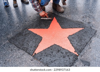 Worker finishing the installation of a star on the Hollywood Walk of Fame, top-down view.