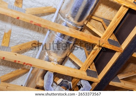 Worker are fitting thermal barrier insulation around metallic duct in new home ceiling.
