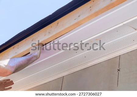 Worker is fitting vinyl PVC soffit panels under roof edge of house work is being done