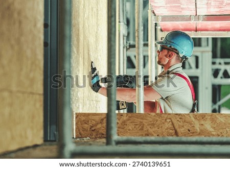 A worker is fitting a wall while on a construction site in the afternoon sun.