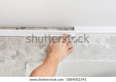Worker fixes the plastic molding to the ceiling. Installation of ceiling cornice.