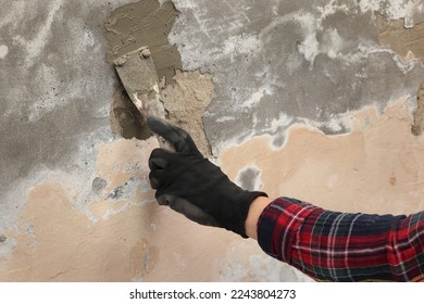 Worker fixing cracks and damages on wall, hand in glove spreading plaster using trowel