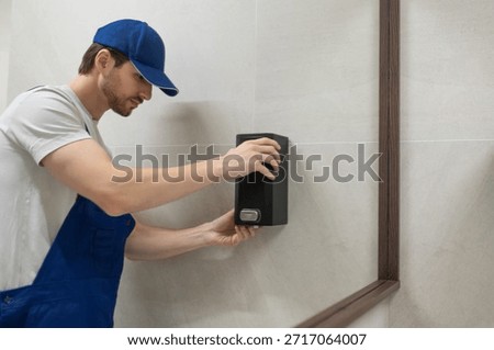 Worker fixing wall mounted soap dispenser in modern bathroom