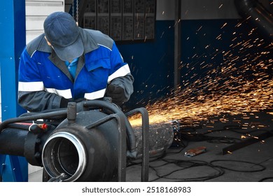 A worker is focused on grinding a metal pipe in a workshop setting. Sparks fly as the tool makes contact, illuminating the space. The worker is dressed in safety gear, demonstrating skill and concentr - Powered by Shutterstock