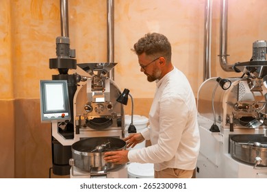 Worker is focused on the roasting machine, skillfully managing the process of preparing arabica and robusta coffee beans in a workshop setting with various coffee equipment.