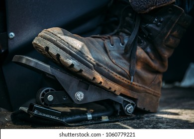 Worker foot in large shoe or boot presses on pedal of industrial excavator or tractor
