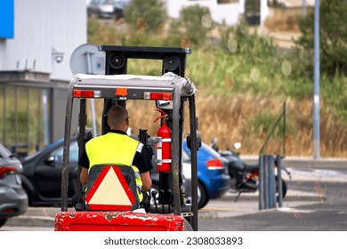 A worker with a forklift driving on the street