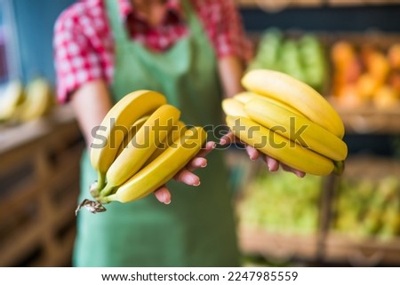 Worker in fruits and vegetables shop is holding bananas. Close up of bananas.