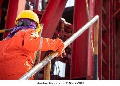 A Worker With Fully Ppe And Orange Coverall Is Holding Handrail During Walking Up To The Drilling Rig Platform. Oil Field Industrial Working Action Photo, Partial Focus At The Person's Hand Part.