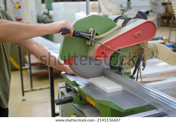 Worker in a furniture factory cutting a\
piece of white wood with a circular\
saw\
