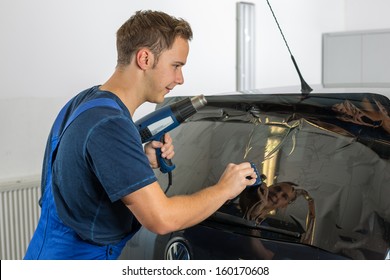 Worker In Garage Tinting A Car Window With Tinted Foil Or Film