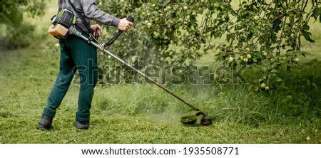 Worker with a gas mower in his hands, mowing grass in front of the house. Trimmer in the hands of a man. Gardener cutting the grass. Lifestyle Foto d'archivio © 