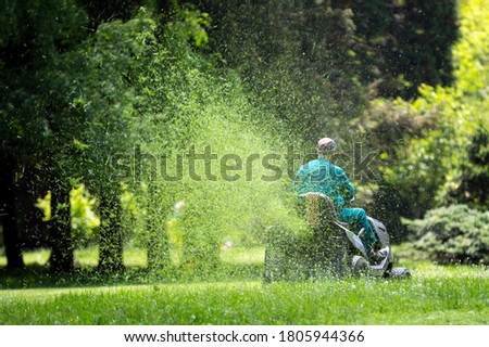 Worker with a gasoline tractor lawn mower mows the fresh green lawn.