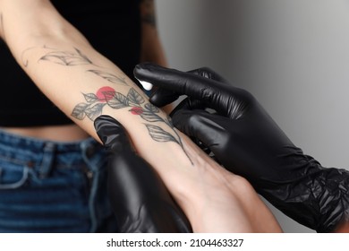 Worker in gloves applying cream on woman's arm with tattoo against light background, closeup - Shutterstock ID 2104463327