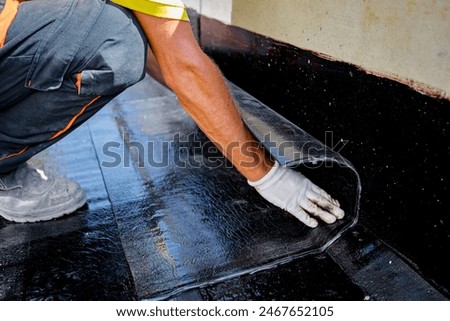 Worker in gloves prepare for melting, manually place and unroll rolled up, sheet of waterproofing installation over concrete. Residential building under construction placing water insulation