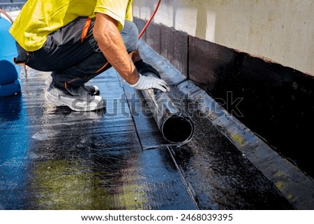 Worker in gloves prepare for melting, manually place and unroll rolled up, sheet of waterproofing installation over concrete. Residential building under construction placing water insulation