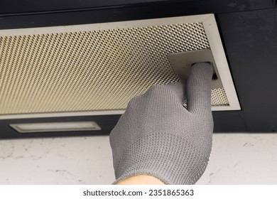 Worker in gloves removes aluminum grease filter from kitchen hood. Concept of cleaning, kitchen maintenance, hygiene, air quality, ventilation, grease buildup, replacing filters