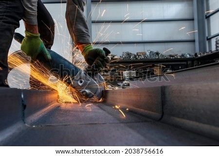Worker is grinding and cutting to steel material with manual metal cut off wheels in the workshop. Grinding produces sparks and little fragments of metal.