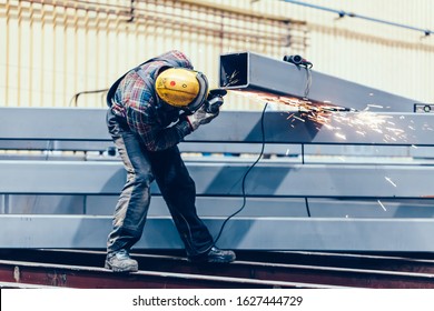 Worker grinding a steel profile in factory. Heavy industry at shipyard - Powered by Shutterstock