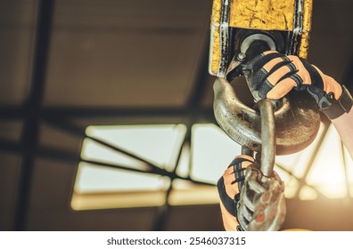 A worker grips a heavy lifting hook in a bright industrial warehouse, showcasing strength and teamwork in action. - Powered by Shutterstock