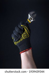Worker hand in glove holds adjustable wrench on a dark background. Idea for building or renovation