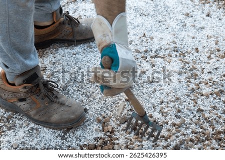 Worker hand in  gloves holding rake leveling surface of gravel in yard to prepare it for stone plates 