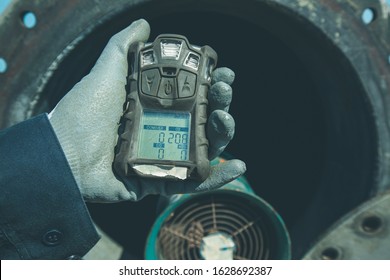 Worker hand holding gas detector inspection safety gas testing at front manhole tank to work inside confined