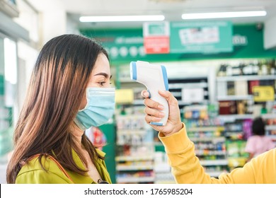 Arbeiter Hand, die Temperaturscanner hält Fieber von Kunden, die Schutzmaske tragen, bevor sie im Supermarkt einkaufen 