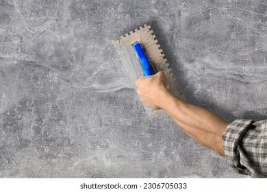 worker hand with steal trowel plastering cement on wall