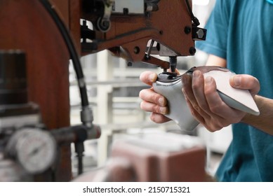 Worker handling dummy female high heel shoe under industrial machinery in a production line