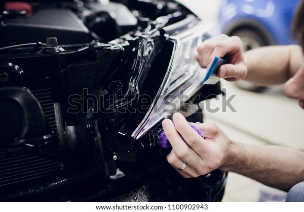 Worker hands installs car paint protection film\
wrap headlamp