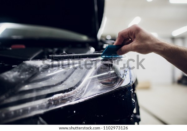 Worker hands installs car paint protection film\
wrap auto headlight