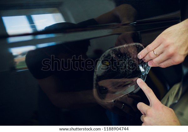 Worker\
hands installs car paint protection film\
wrap.