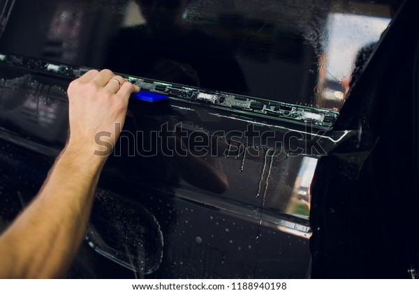 Worker\
hands installs car paint protection film\
wrap.