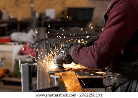 Worker hands operating angle grinder on steel with shower of bright sparks and blurred workshop background